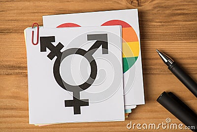 Top view photo of rainbow flag and black transgender symbol on stickers and pen on wooden table background Stock Photo