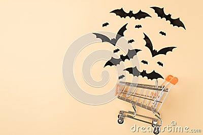 Top view photo of shopping cart model with flying bats silhouettes on isolated beige background with copyspace Stock Photo