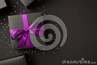 Top view photo of stylish black gift boxes with purple ribbon bow and sequins on black background with copyspace Stock Photo