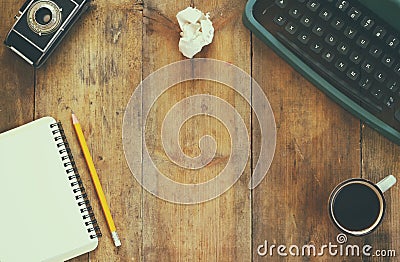 Top view photo of vintage typewriter, blank notebook, cup of coffee and old camera on wooden table. retro filtered image Stock Photo