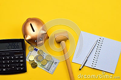 Top view of a piggy bank on a yellow surface with coins, a banknote, hammer, calculator, notebook Stock Photo