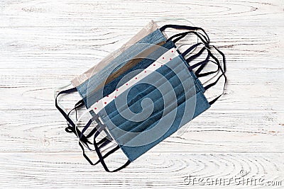 Top view of a pile of homemade textile reusable masks on wooden background. Respiratory protection concept with copy space. DIY Stock Photo