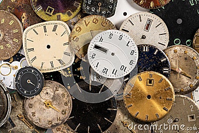 Top view on pile of old worn clock dials. Aged scratched round watch faces with hands and numbers. White, black and Stock Photo