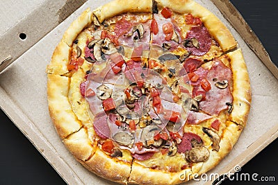 Top view, pizza with bacon, tomatoes, salami, cheese and mushrooms in a cardboard box on dark background. From above, Stock Photo