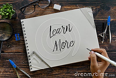 Top view of plant,sunglasses,magnifying glass,stationery and hand holding pen writing Learn More on notebook Stock Photo