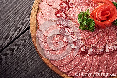 Top view of plate of sliced sausage decorated with aromatic herbs. Sausage on wooden catering platter, flat lay of meat Stock Photo