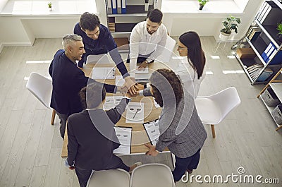 Top view of a positive group of colleagues holding hands as a symbol of cooperation and support. Stock Photo