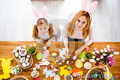 Top view of pretty beautiful mummy teaching her cute joyful small daughter paint decorate easter eggs together wearing rabbit cos Stock Photo