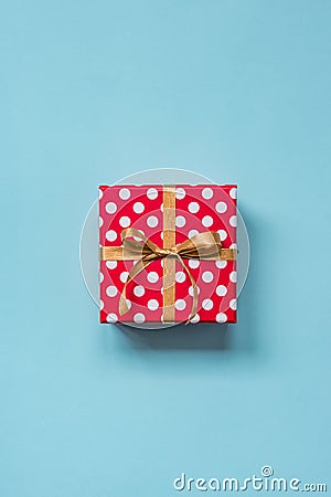 Top view of a red dotted gift box tied with golden bow over blue background. Stock Photo