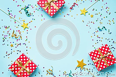 Top view of a red dotted gift boxes, golden magic wands, colorful confetti and ribbons over blue background. Celebration concept. Stock Photo