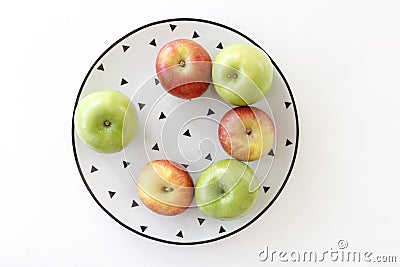 Top view of Red and green apples in white plate with black triangles pattern on white background Stock Photo