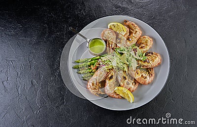 Top view of roasted shrimps served with asparagus and lemon on black background Stock Photo