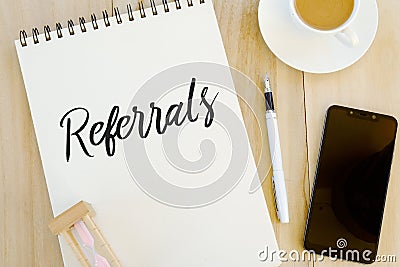 Top view of sand clock,pen,mobile phone,a cup of coffee and notebook written with Referrals. Stock Photo