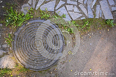 Top view of sand, grass, paved path and manhole in the rays of the rising sun Stock Photo