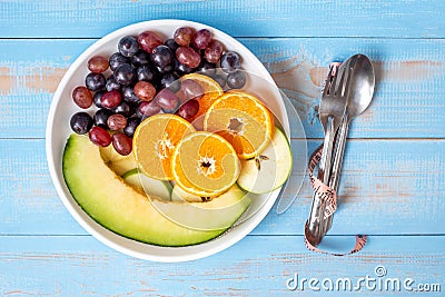 Top view spoon and fork, black grapes, red grapes, Valencia orange and melon fruits in white dish with pink Measuring tape on blue Stock Photo