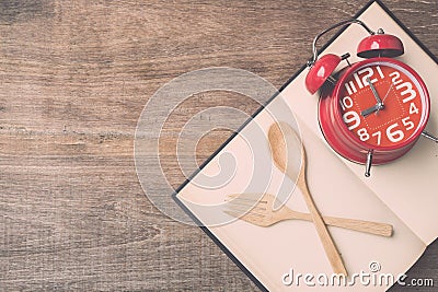 Top view spoon, fork, book and red clock on wooden plank background Stock Photo