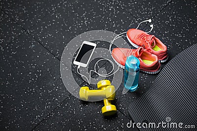 A top view of sportive accessories for gym training. Sport shoes, dumbbells, bottle, and a white phone on a black Stock Photo