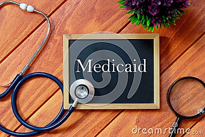 Top view of stethoscope,magnifying glass,plant and blackboard written with Medicaid on wooden background. Health concept. Stock Photo