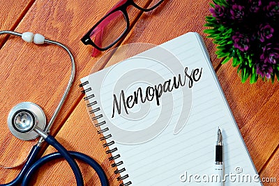 Top view of stethoscope,pink eyeglasses,plant,pen and notebook written with Menopause on wooden background.Health concept. Stock Photo