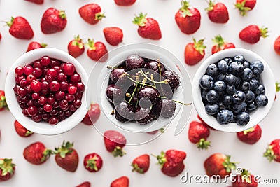 Top view of sweet blueberries, cherries and cranberries on bowls and strawberries on background. Stock Photo