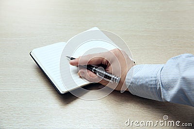 Top view of the table where there is a clean pocketbook. Women`s right handed hold a pen Stock Photo