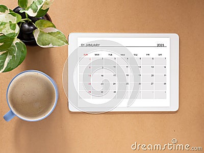 Top view, tablet showing January 2023 calendar page and tree, coffee cup. Stock Photo