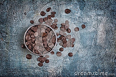 Top view of dark chocolate drops or morsels in bowl on blue concrete background Stock Photo