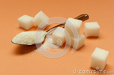 Closeup of teaspoon full of sugar and pile of sugar cubes on the orange background Stock Photo