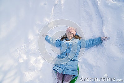 A teen girl in a blue coat tries to move on a sledge from a snow slide and falls Stock Photo
