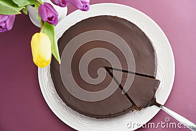 Chocolate cake on a purple table and a bouquet of puprle and yellow tulips. Top view Stock Photo