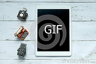 Top view of toys camera,typewriter and tablet written with GIF on white wooden background. Stock Photo