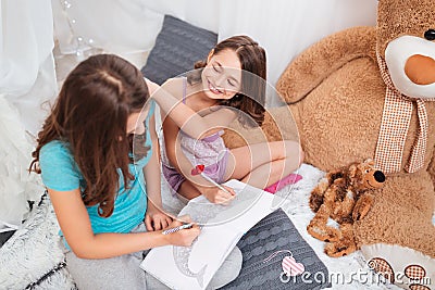 Top view of two cheerful charming sisters sitting and colouring Stock Photo