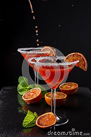 Top view of two cocktail glasses with drops of blood orange martini, half orange and mint, on black background, vertical Stock Photo