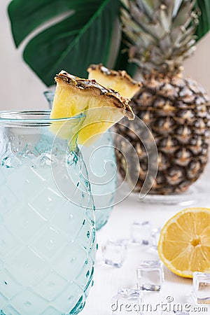 Top view of two glasses with lemon juice with pieces of pineapple on white wooden table with half a lemon, ice and pineapple, on w Stock Photo