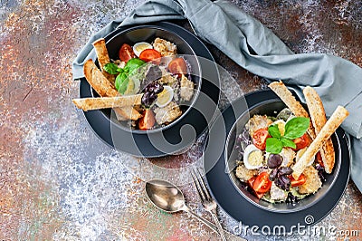 Top view two servings of Caesar salad with chicken, quail egg, cherry tomatoes, croutons and basil in dark blue bowls on a rusty Stock Photo