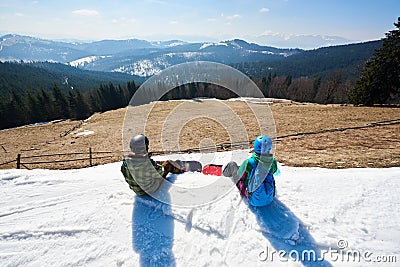 Back view of two tourists snowboarders on background of blue sky and mountains on sunny winter day. Stock Photo