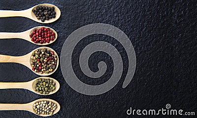 Top view of 5 types of peppercorn in a wooden spoon on a black background Healthy food concept Stock Photo