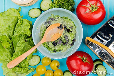 top view of vegetable salad with lettuce cucumber tomato coriander and grater with wooden spoon on blue background Stock Photo