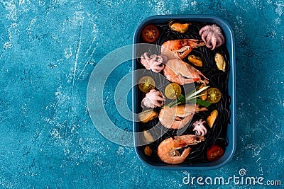 Top view vegetarian black spaghetti with king prawns, mussels, octopus and vegetables in blue plate on blue background Stock Photo