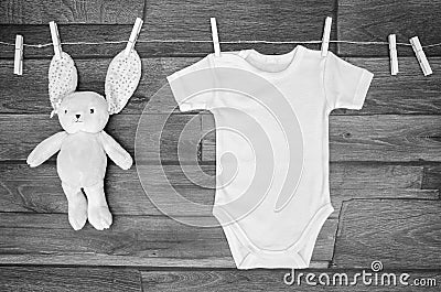 Top view white baby bodysuit on a clothesline with teddy hare on a wooden background. Copy space for text mockup Stock Photo