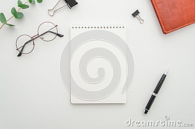 Top view of white office desktop with blank spiral notepad, glasses, supplies and leather wallet. Mock up Stock Photo