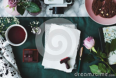 Top view of white paper sheets, coffee, rose, stamps, cake, camera on a green background Stock Photo