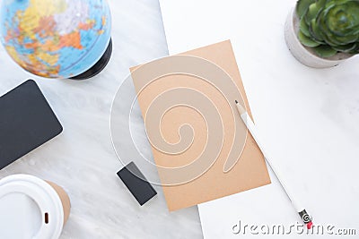 Top view of white pencil on brown paper with blue globe,blackboard,coffee cup and plant on marble table.new yearâ€™s resolutions Stock Photo