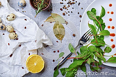 Closeup of a table with bay leaves, green salad leaves, quail eggs, a half of lemon on a light gray background. Stock Photo