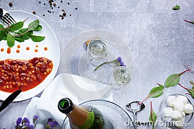 Close-up of a bottle of champagne, white plate with canned beans, garlic, almond, tomatoes on a light background. Stock Photo