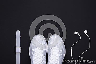 White sport shoes sneakers with smart watch activity tracker and earphones headphones on black color background. Stock Photo