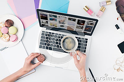 top view of woman drinking coffee with macaroon while using laptop Editorial Stock Photo