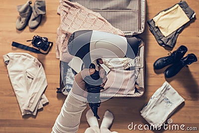 Top view on the woman holds hair dryer packing clothes in the open suitcase. Travel Stock Photo