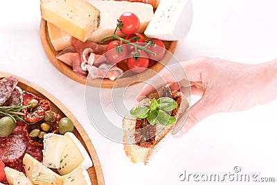 Top view on woman`s hand holding bruschetta with sun dried tomatoes above table with traditional antipasti plates Stock Photo