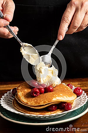 Top view of woman`s hands with spoons and mascarpone cheese on pancakes with cherries Stock Photo